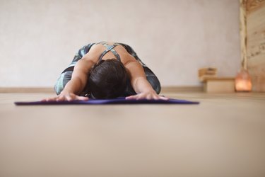 A person on a yoga mat with their arms and hands outstretched in child's pose as an example of an exercise that can help with pelvic floor health for people with vaginas