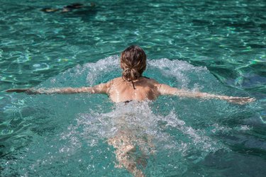 a young woman doing a swim cardio workout on top of pool water, back view