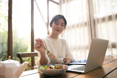 Young woman eating lunch while working with laptop