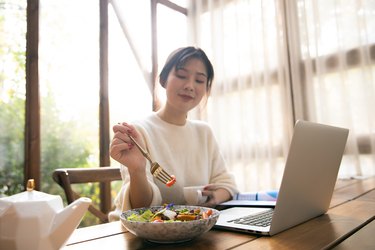 年轻女子一边吃午餐一边用笔记本电脑工作