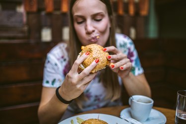Woman eating a burger, thinking about how it will make her feel uncomfortable after