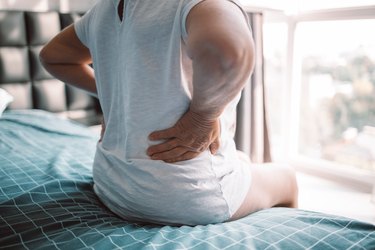 closeup rear view of a woman with her hands on her lower back, sitting in bed