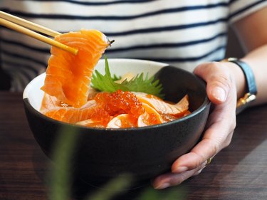 close up of woman using chopsticks in bowl of salmon sashimi