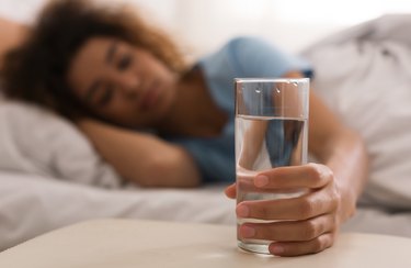 Woman's hand taking glass of water in bed, as a natural remedy for snoring