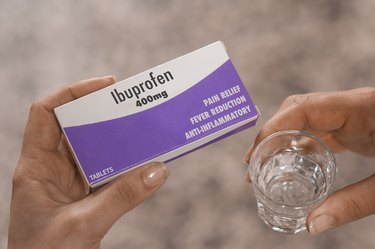 A person holding a box of 400mg ibuprofen tablets in their hand and a glass of water