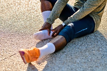 person sits on pavement and holds heel of foot due to plantar fasciitis pain