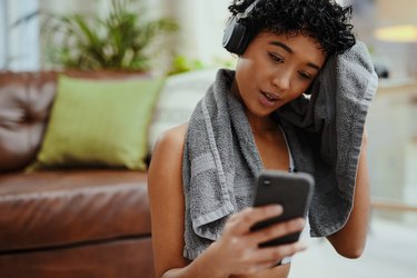 Woman with post-workout sweat, drying herself with a towel while looking at her phone