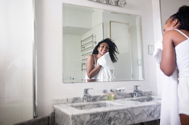 woman looking in the bathroom mirror and drying her face with a towel