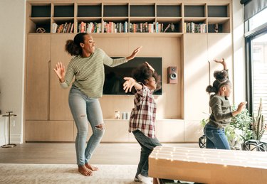 a mother and two kids dance in their sunny living room