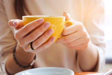 Yellow coffee mug in the hands of a young woman wondering, "How long does it take to break a caffeine addiction?"