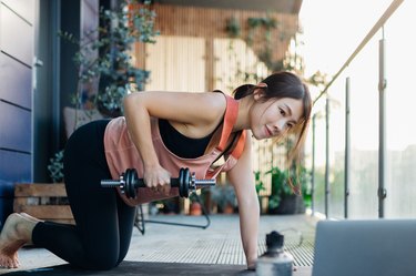 fit Asian woman doing a dumbbell row with adjustable dumbbells on her balcony