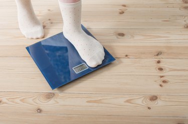 a child's feet in white socks stepping onto a blue bathroom scale on a hardwood floor