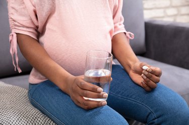 Black pregnant person sitting on couch holding glass of water and Eplazyme pill wondering about Glutenease and Atomy Finezyme side effects