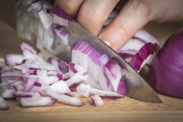 closeup of chef chopping a red onion with a knife