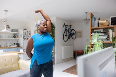 Older adult wearing a blue tank top and black leggings doing a full-body resistance band workout in living room.