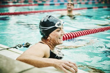 Laughing mature swimmer resting between sets of early morning 30-minute swim workout for beginners in pool
