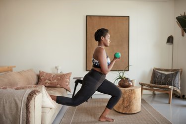 Black woman doing a low-impact strength training workout with dumbbells in he rliving room