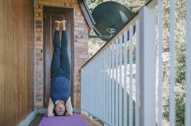 mid adult practicing yoga headstand on a balcony