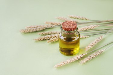 vitamin E-rich Wheat Germ Oil in glass jar and ears of wheat on a light green background.