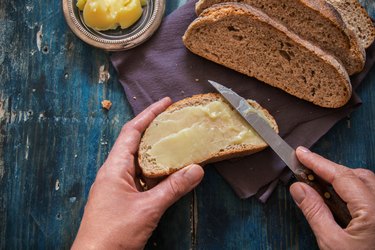 Hands spread fresh butter on whole-wheat bread