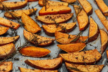 A diabetes-friendly side dish of baked sweet potato wedges on a silver baking tray, sprinkled with herbs and spices.