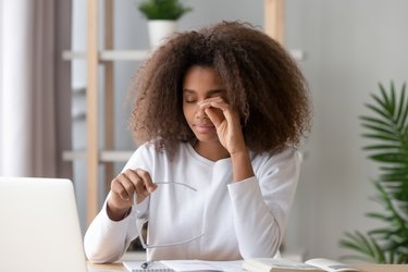 woman working at her desk and rubbing her eyes because she has dry eye