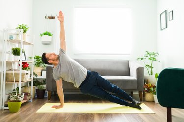 Person wearing a gray T-shirt and navy blue sweatpants doing a side plank on yoga mat in living room to demonstrate yoga poses for scoliosis