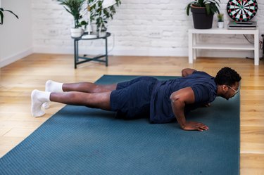 Adult doing push-up exercise in living room on blue mat