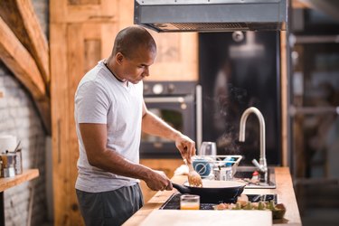 man preparing scrambled eggs for breakfast in kitchen