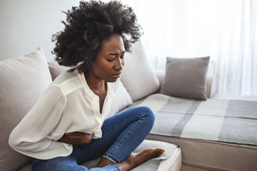 Sad beautiful woman sitting on the couch and feeling spasm and symptoms of pms.