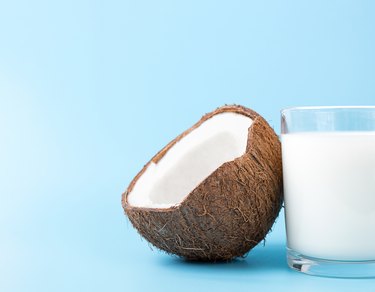 Coconut Milk in a glass and coconut on blue background with copy space