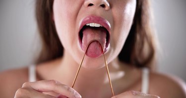 Close view of a person using a tongue scraper on their tongue to clean it