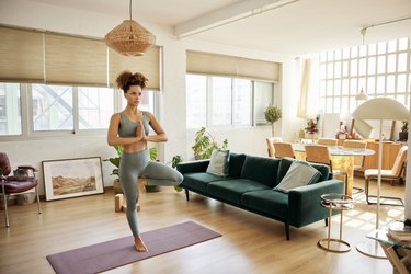 woman practicing tree pose on a purple yoga mat in her living room