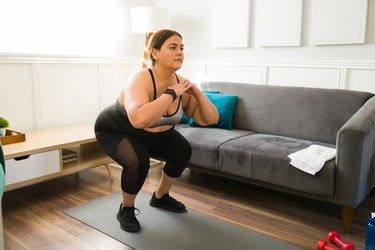 Person doing squats in living room on yoga mat.