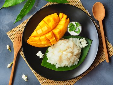Nutritious mango and sticky rice dessert on a plate next to wooden utentils