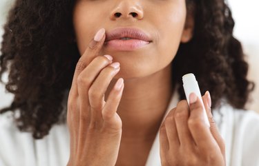 Unrecognizable woman applying lip balm to treat her chapped lips