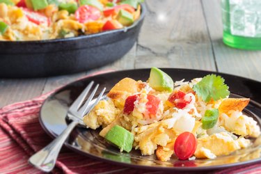 Egg scramble with avocados, tomatoes and cheese, on black plate on wooden table.
