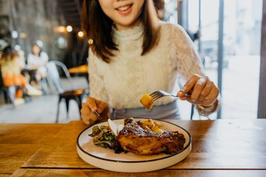 Asian woman enjoying a whole chicken leg meal in a cafe