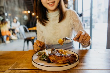 一名亚洲妇女在咖啡馆享用全鸡腿餐