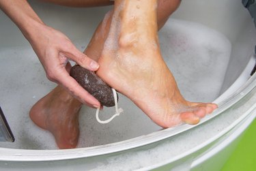 close view of a person using a pumice stone on their heel, as an example of how to get rid of calluses on feet