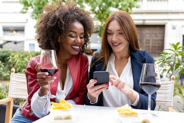 Two adults drinking red wine outside and looking at a smartphone together