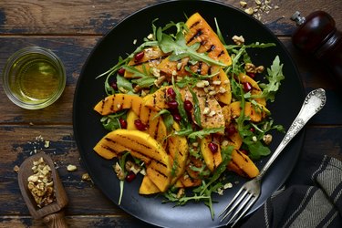 Grilled pumpkin warm salad with arugula, walnuts and pomegranate seeds on black plate