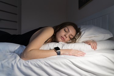 Person in a black tank top lying in bed and wearing a smartwatch to track their heart rate while sleeping