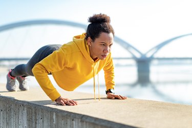 African American woman wearing a yellow hoodie and doing push-ups outdoors
