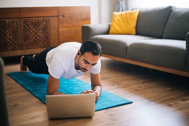 Man uses laptop while performing a forearm plank
