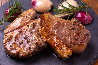 Cooked bone-in lamb loin on a plate with garlic and rosemary