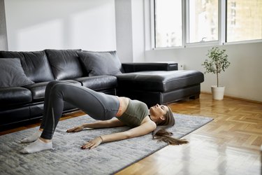 young caucasian woman doing a glute bridge with hamstring curl in her living room