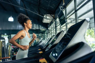 Young athlete running on treadmill at the gym in light blue top and leggings.