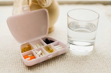 Pink container holding several vitamins next to a glass of water