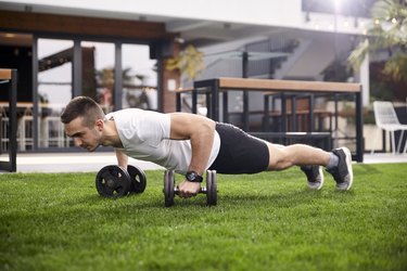 fit man doing a dumbbell push-up outside on the grass